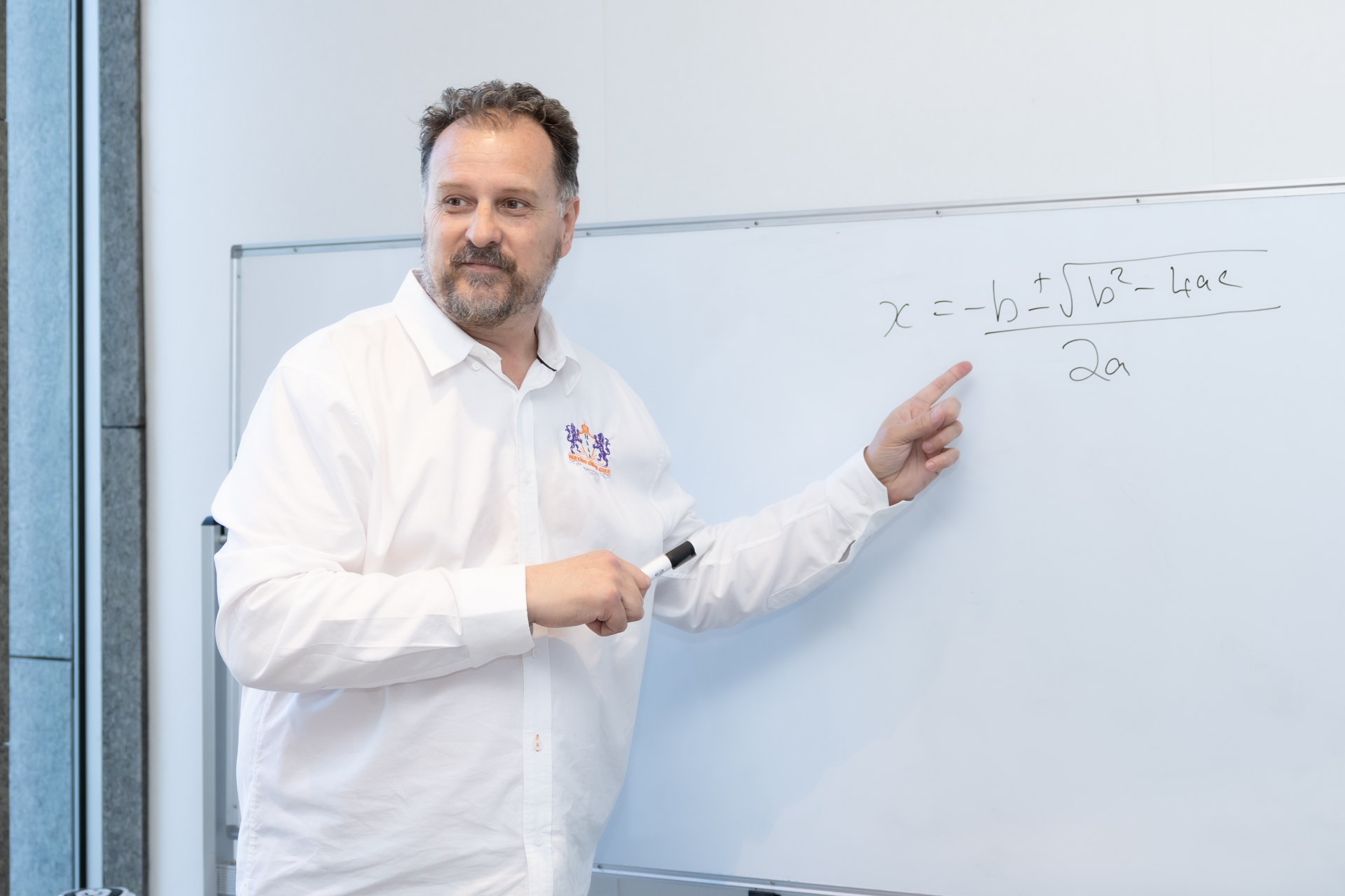 Juan pointing at the quadratic formula on a whiteboard